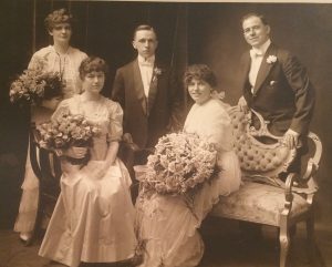 14Mystery Bridesmaid Finally IdentifiedJean PollyOnondaga CountyFor years, I have been flummoxed by this lovely studio portrait of my great aunt’s wedding party, taken 16 June 1915 in Brooklyn NY. That’s her in front, her lap covered by a huge bouquet of roses whose fragrance must have been divine. The groom in the center had to be satisfied with a tiny sprig in his lapel!
To the right is my grandfather, brother of the bride, and far left is his wife, my grandmother. But the name of the young bridesmaid in front was unknown.
I posted the photo in my great aunt’s profile in my family tree on Ancestry. It was not long before I heard from a woman in Chicago, who had a copy of the same photo and identified the young girl as the bride’s 21-year- old first cousin. And she knew all this because the bridesmaid later became her mother!
Better yet, she was able to tell me all about this branch of the family, of which I knew nothing. 
Possible family activity over Zoom: hold up old photos and see if anyone can identify the faces, then label with pencil or acid-free pen. Your descendants will thank you!